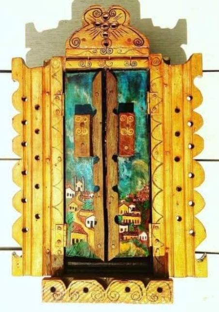 Oratório amarelo fechado, de contorno recortado com furos, com casario e uma igreja sob céu turquesa pintados nas portas