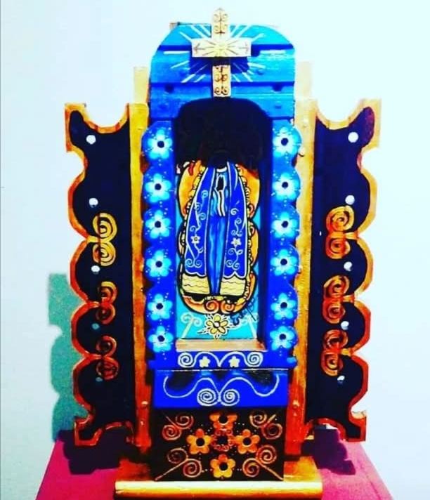 Oratório azul aberto com Nossa Senhora Aparecida no nicho entre flores, cruz no alto e portas pretas com espirais