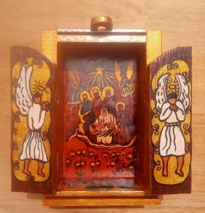 Oratório aberto com o presépio sob uma estrela, em fundo vermelho, e um anjo sobre dourado em cada porta