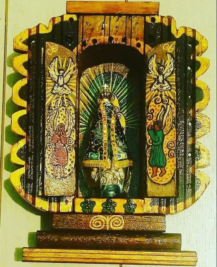 Oratório aberto, preto e amarelo, de contorno recortado, com Nossa Senhora Aparecida entre raios verdes e anjos nas portas